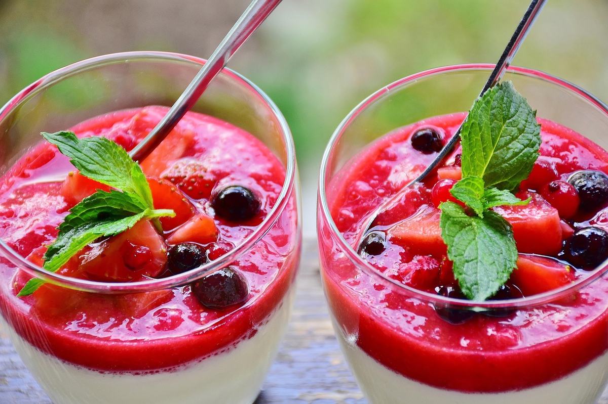 Zwei Gläser Panna cotta mit rotem Beeren-Fruchtspiegel, Blaubeeren und Minze