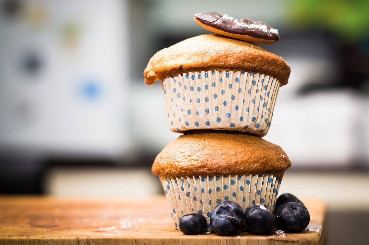 Zwei gestapelte Muffins in gepunkteten Papierförmchen, davor Blaubeeren