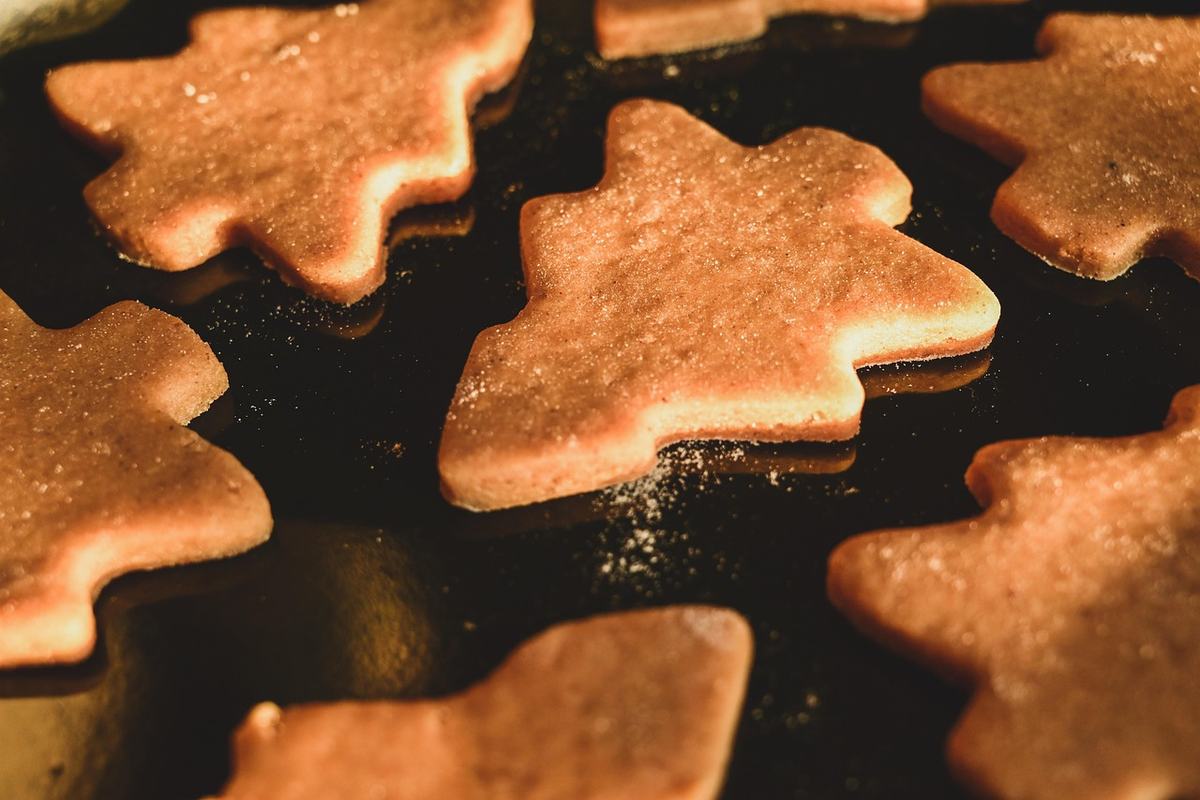 Flache Lebkuchen in Tannenbaumform auf dunklem Backblech