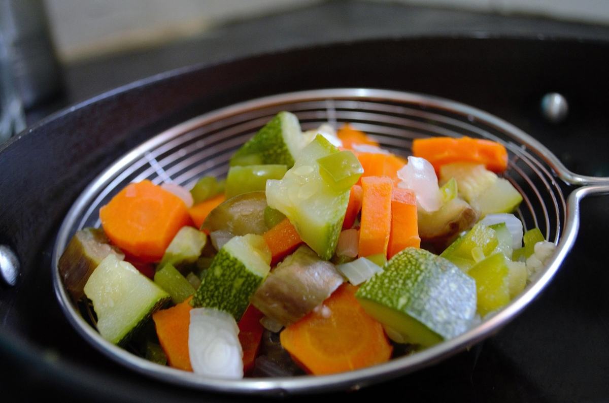 Gewürfeltes, blanchiertes Gemüse aus Möhren und Zucchini in einem Drahtsieb über dem Topf