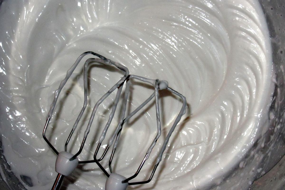 Glänzender, gezuckerter Eischnee mit den Rührbesen eines Handrührgeräts in einer Metallschüssel