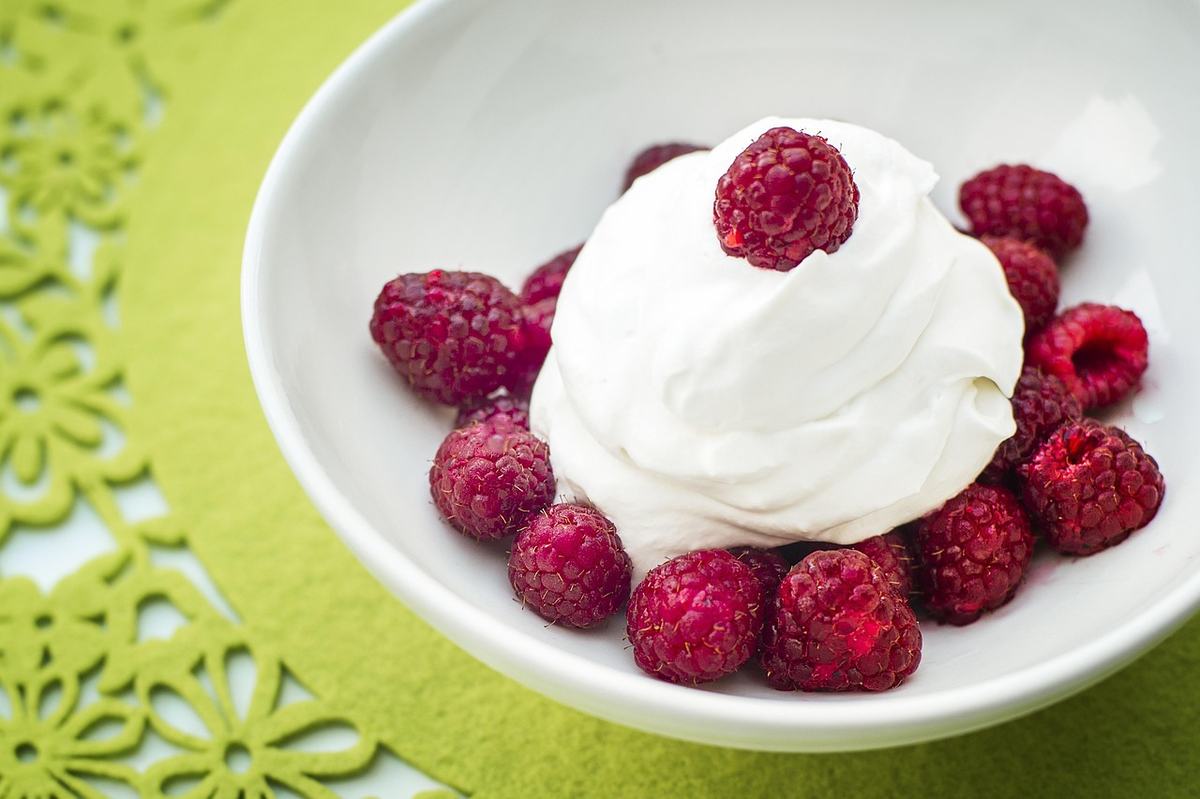 Weiße, steif geschlagene Sahne mit frischen Himbeeren in einer weißen Schale