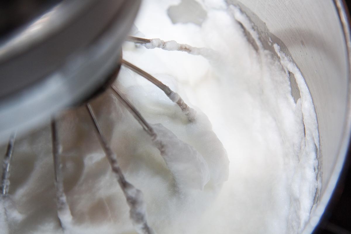 Steif geschlagener Eischnee am Schneebesen einer Küchenmaschine in einer Edelstahlschüssel