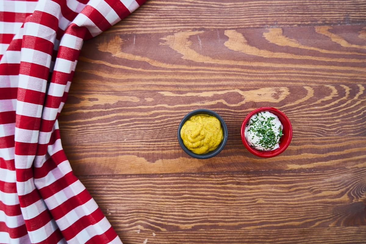 Zwei Schälchen auf einem Holztisch, eines mit Senf, eines mit Mayonnaise und Kräutern