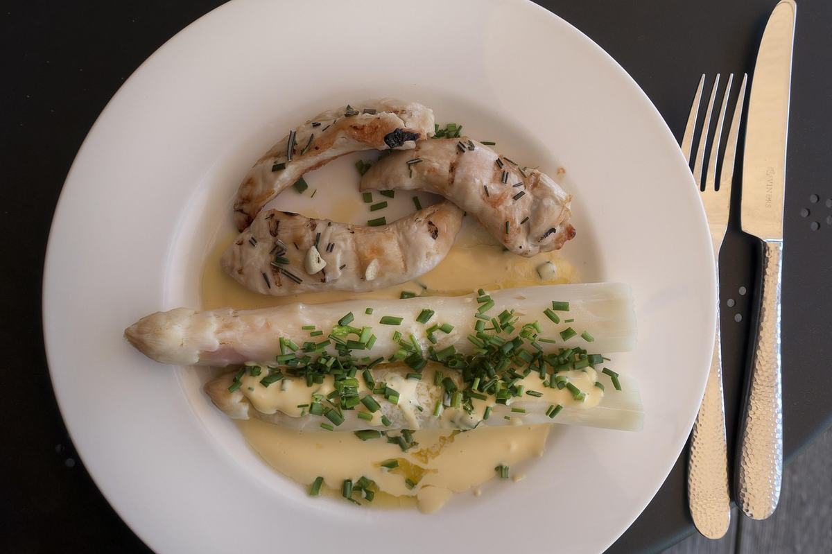 Weißer Spargel mit Sauce Hollandaise und Schnittlauch, daneben gegrilltes Hähnchen auf einem weißen Teller