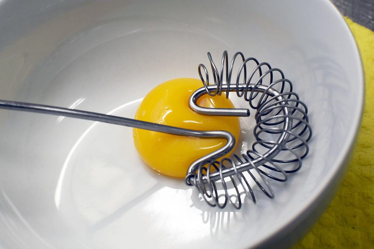 Rohes Eigelb mit einem Spiralschneebesen in einer weißen Schüssel