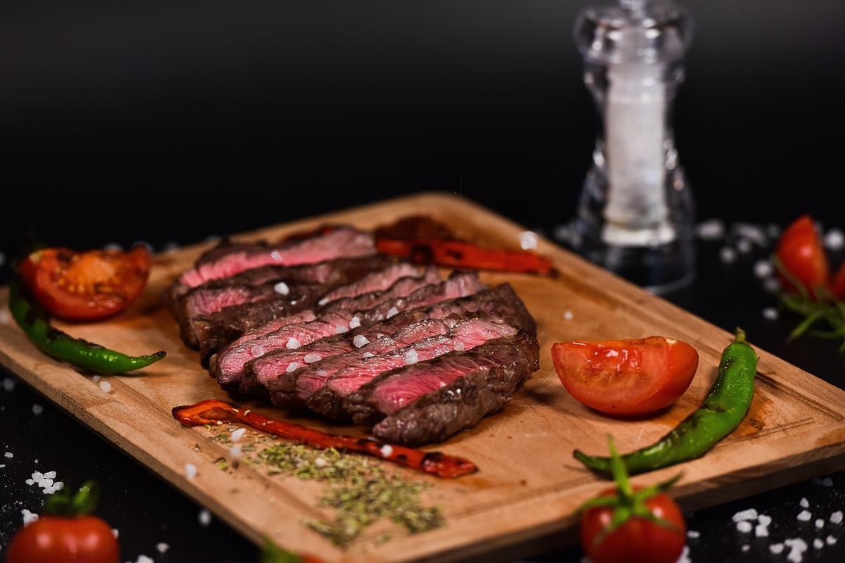 Aufgeschnittenes Rindersteak, innen rosa, auf einem Holzbrett mit Tomaten und Chilischoten