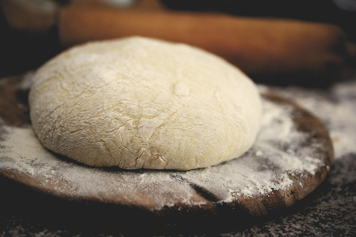 Glatt gekneteter, aufgegangener Hefeteig auf einem bemehlten Holzbrett