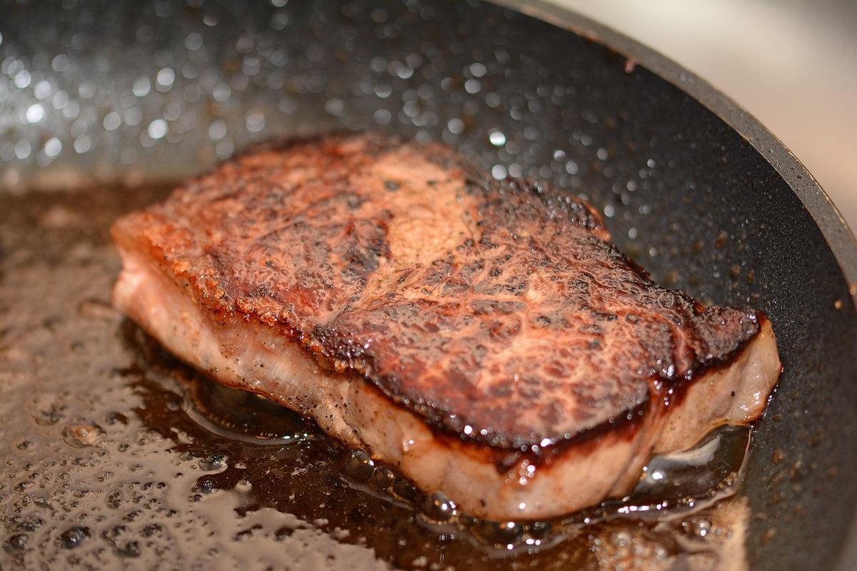 Nahaufnahme eines Steaks mit dunkelbrauner Bratkruste in einer beschichteten Pfanne mit Bratfett