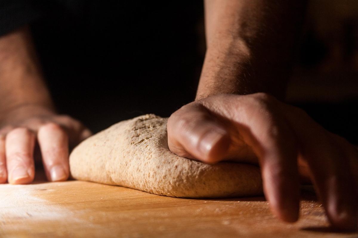 Zwei Hände kneten einen Brotteig auf einer bemehlten Holzfläche