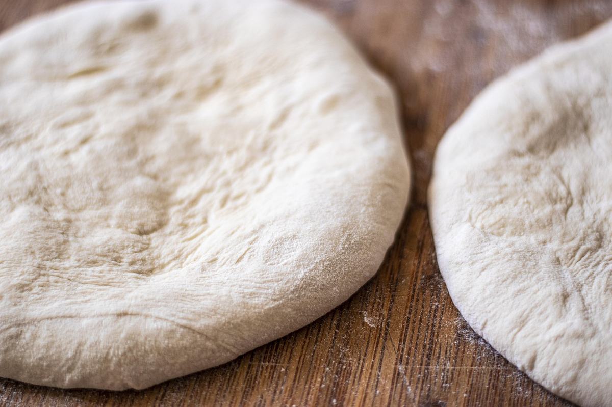 Zwei runde, gegangene Pizzateiglinge auf einer bemehlten Holzplatte