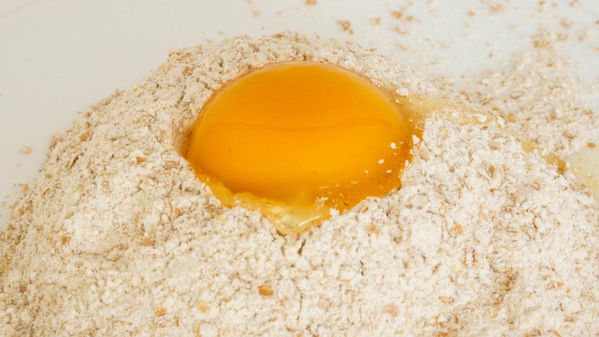 Vollkornmehl mit sichtbaren braunen Schalenteilchen, in einer Mulde liegt ein Eigelb