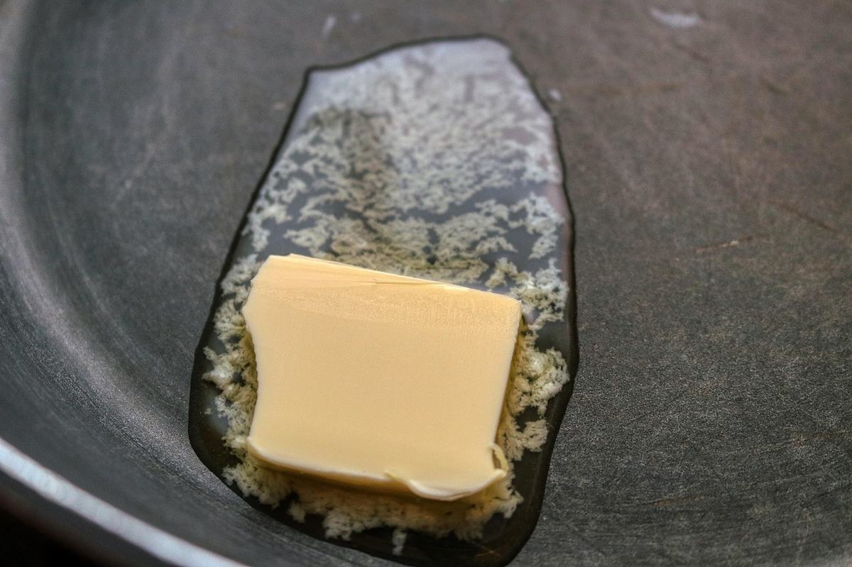 Ein Stück Butter schmilzt in einer dunklen Pfanne, um die Butter herum schäumt es hell
