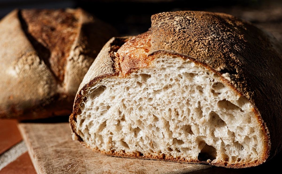 Angeschnittener Sauerteiglaib mit dunkelbrauner Kruste und heller, großporiger Krume auf einem Holzbrett