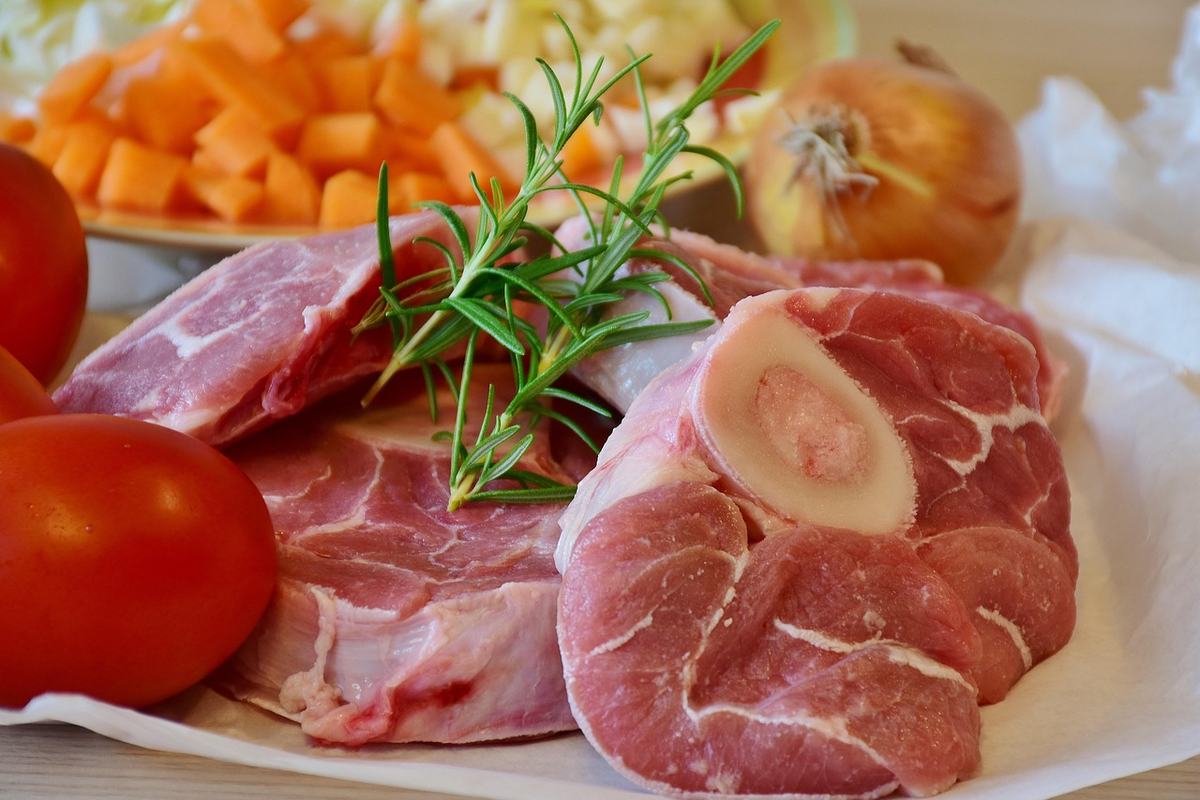 Rohe Beinscheiben mit Markknochen und Rosmarin, dahinter gewürfelte Karotten, Zwiebel und Tomaten