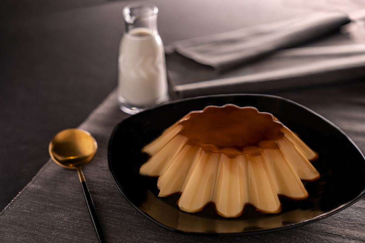 Gestürzte Crème caramel mit bernsteinfarbener Karamellschicht auf einem dunklen Teller
