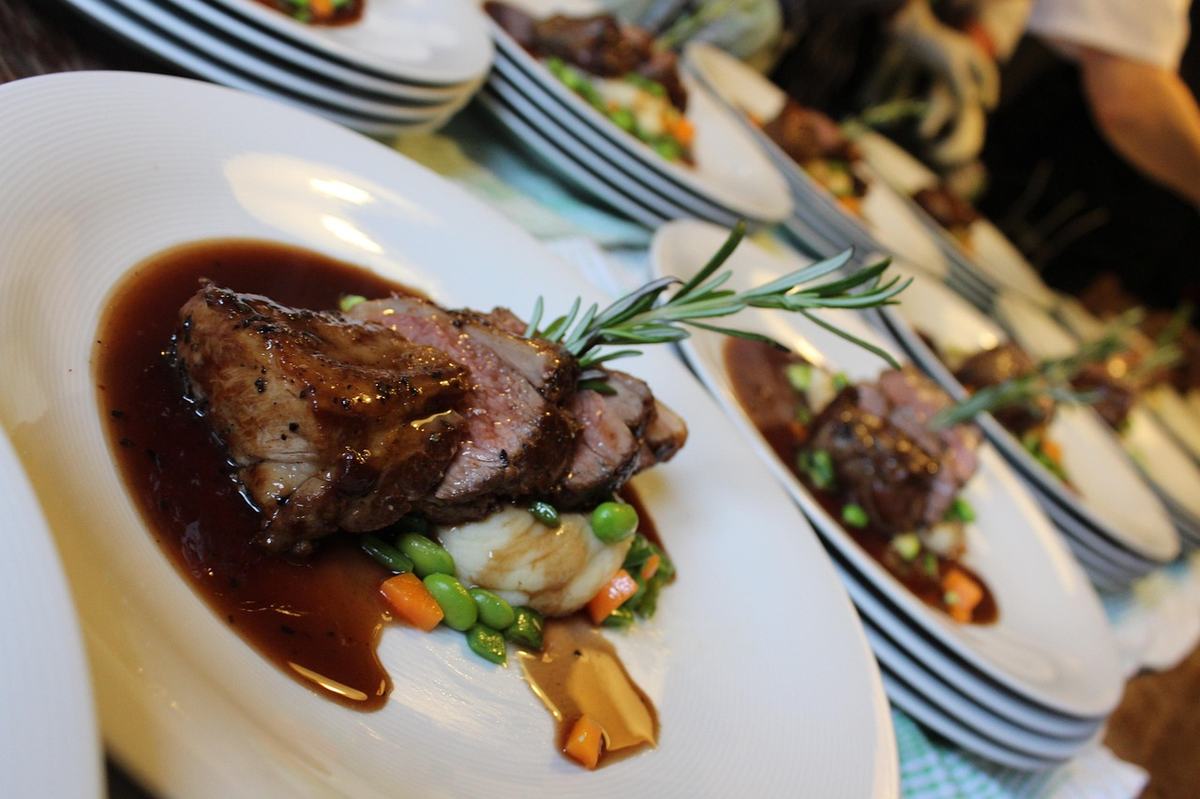 Aufgeschnittener Lammbraten mit dunkler, glänzender Bratensoße, Erbsen und Rosmarin auf einem weißen Teller