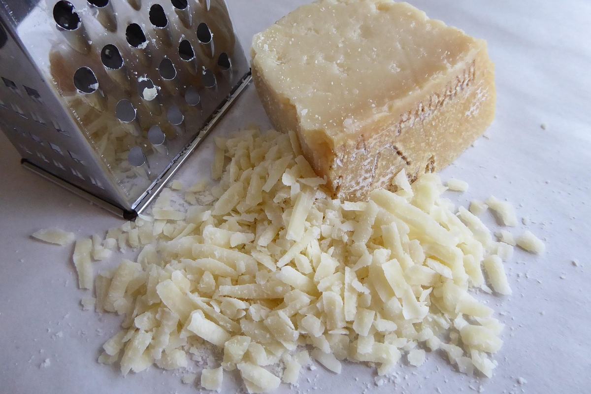 Frisch geriebener Parmesan neben einem Käsestück und einer Vierkantreibe