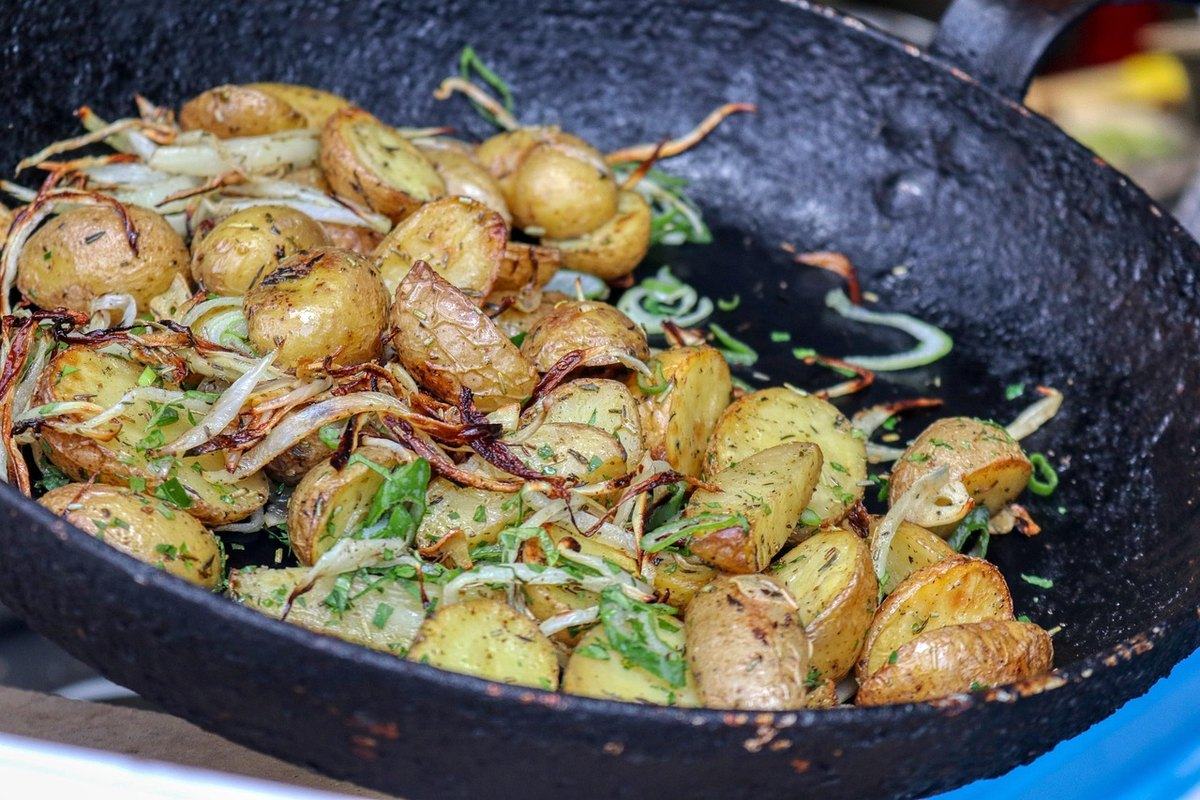 Goldbraun gebratene kleine Kartoffeln mit Zwiebeln in einer schwarzen Eisenpfanne