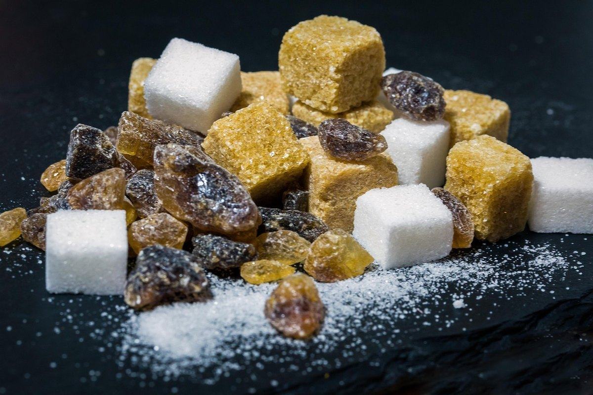 Weiße und braune Zuckerwürfel liegen mit braunem Kandis und Kristallzucker auf dunklem Grund