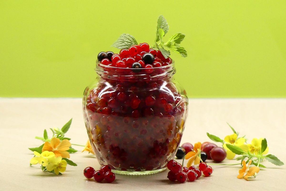 Ein Glas mit Johannisbeerkonfitüre, davor frische rote Johannisbeeren und Blüten